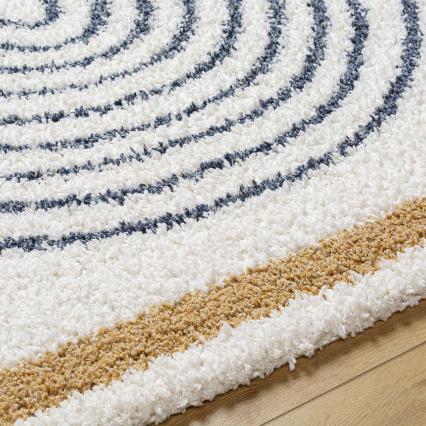 Close up of the Jola Area Rug showing its shag texture and geometric pattern in arctic stone, denim, and camel. Texture