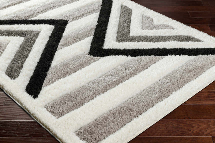 Close up of the Abeje Black & White Area Rug showing its shag texture and geometric black, gray, and off-white pattern. Corner