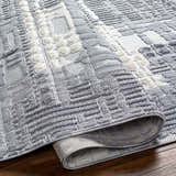 Close-up of the Bodhi Textured Saxony Rug. The gray and white rug has a raised geometric pattern and rolled edge. Fold