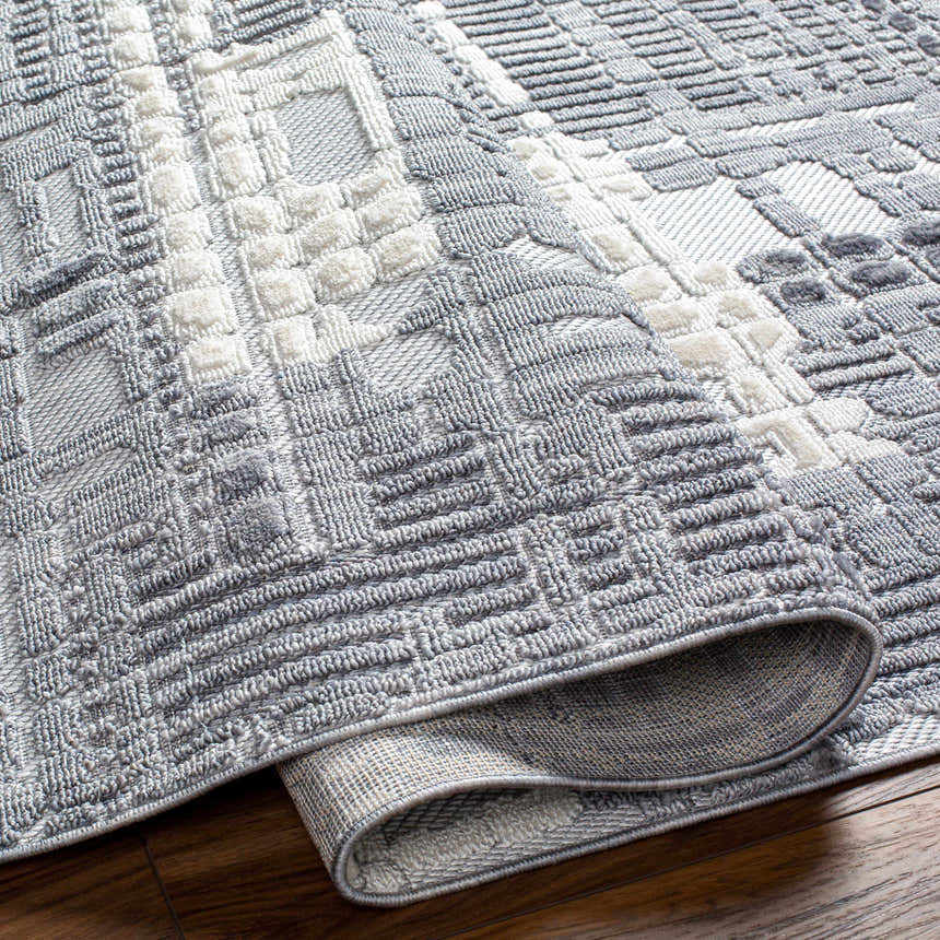 Close-up of the Bodhi Textured Saxony Rug. The gray and white rug has a raised geometric pattern and rolled edge. Fold