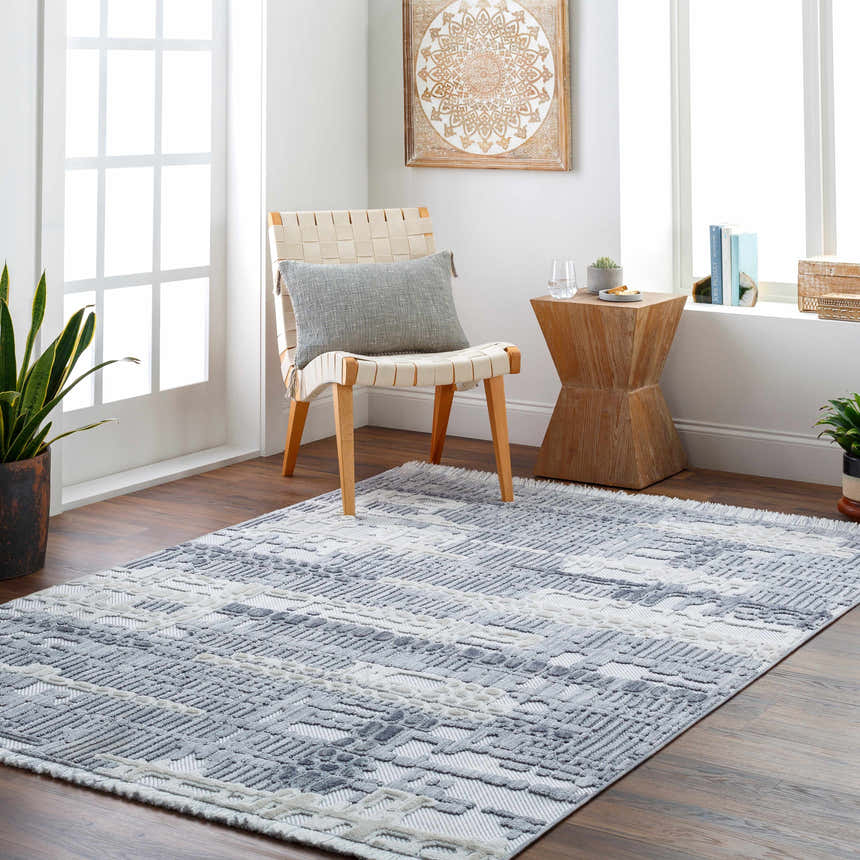 Bright room scene with gray Bodhi Textured Saxony Rug, woven chair, wood side table, and potted plants. Roomscene-Rectangle