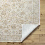 Close-up of the Sashi Tan Luxe Area Rug showing its ash, light silver, and tan traditional floral pattern. Fold
