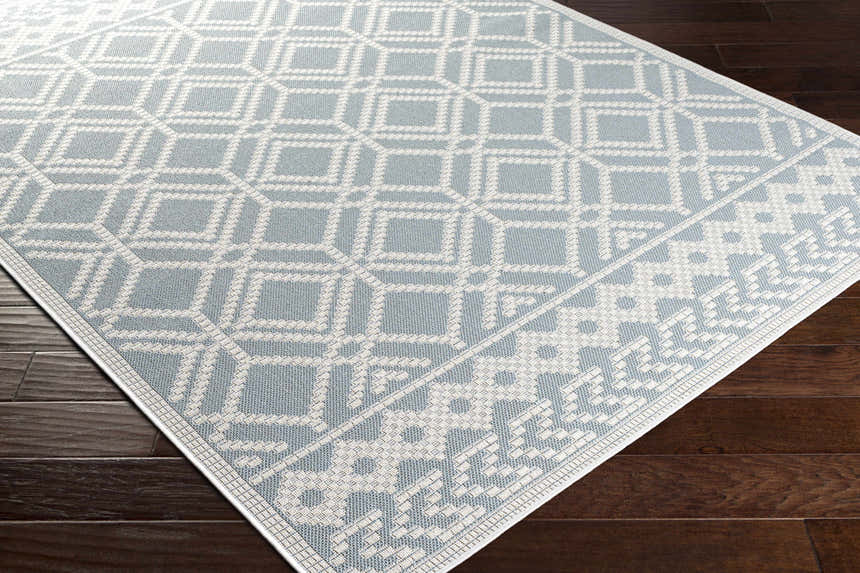 Close-up of the Scawby Area Rug. Light blue rug with a white geometric diamond pattern on dark wood flooring. Corner