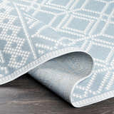 Close-up of the Scawby Area Rug showing a light blue and white geometric diamond pattern and woven texture. Fold