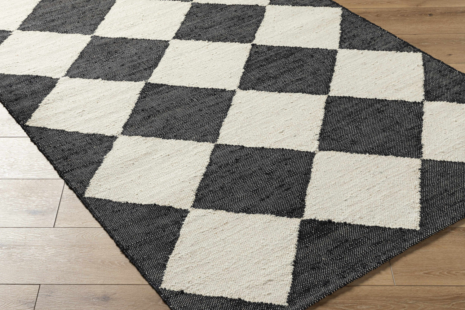 Close-up of the hand woven Sondo Jet Black Area Rug with a bold black and beige checkerboard pattern. Corner