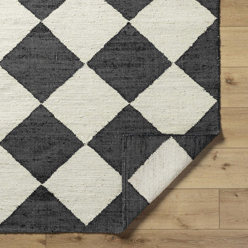 Close-up of the Sondo Jet Black Area Rug. Hand-woven cotton and jute rug with a bold black and beige diamond pattern. Fold