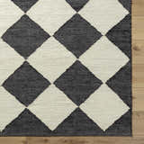 Close-up of the hand woven Sondo Jet Black Area Rug. Features a bold black and beige diamond pattern. Corner