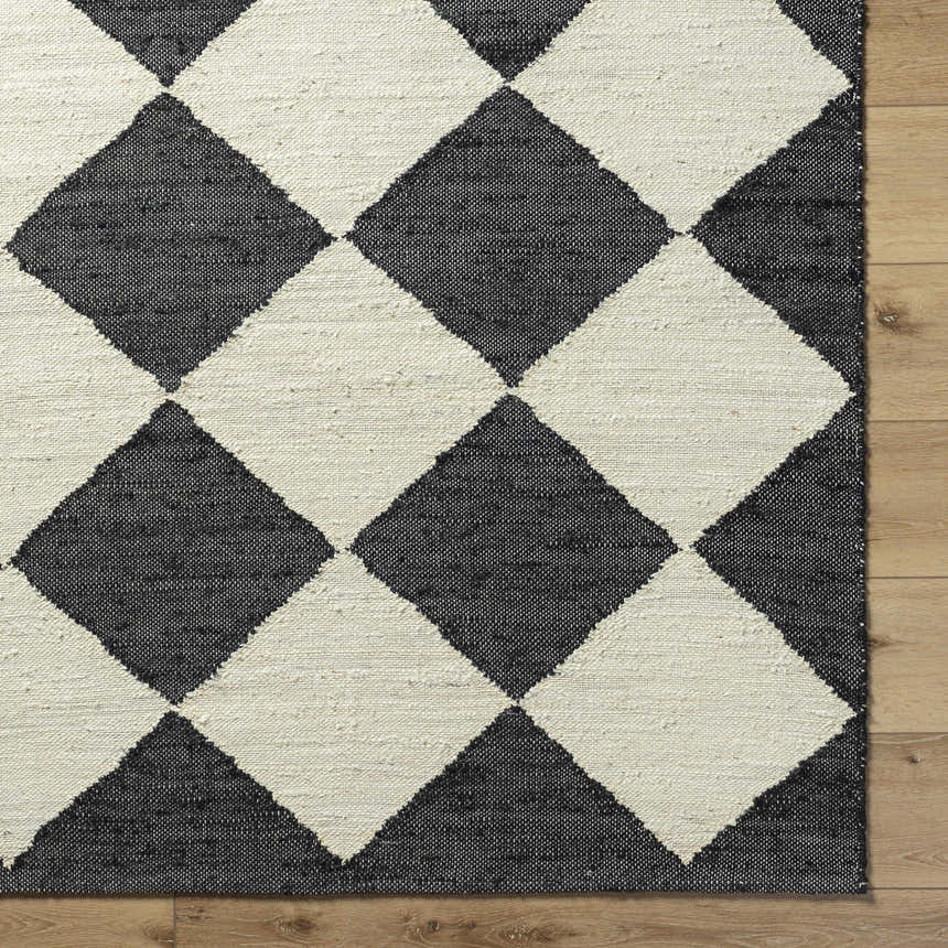 Close-up of the hand woven Sondo Jet Black Area Rug. Features a bold black and beige diamond pattern. Corner