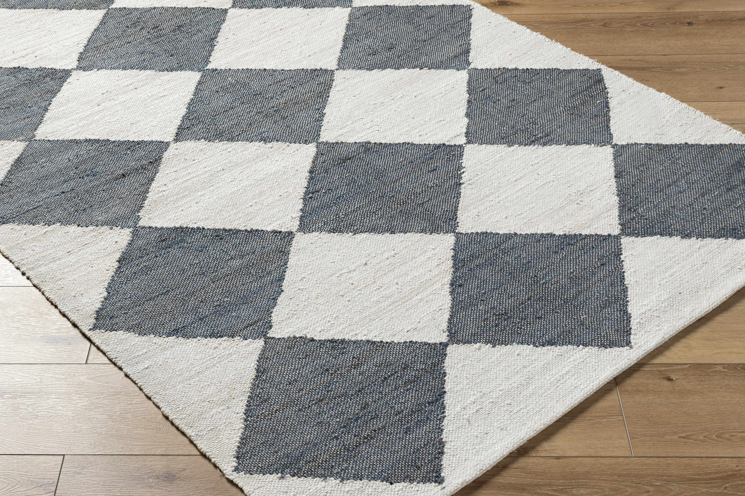 Close-up of Sondo Off White Area Rug showing gray and off white checkerboard pattern and hand woven texture. Corner