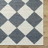 Close-up of the Sondo Off White Area Rug. Features a gray and off white diamond pattern and hand woven texture. Corner