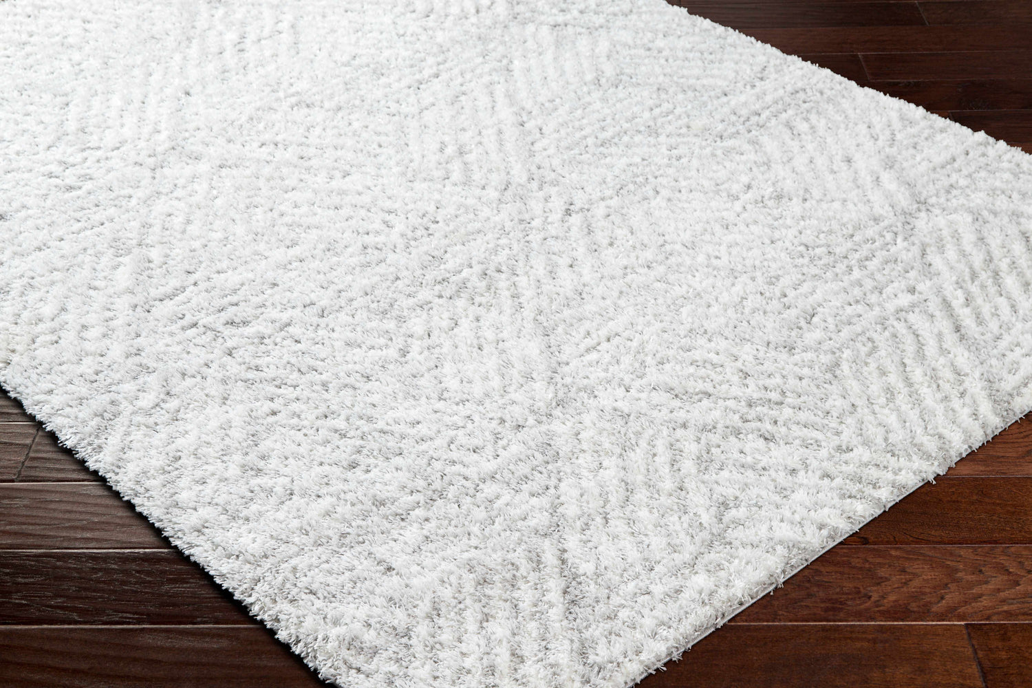 Close-up of the plush Mura Gray Area Rug showing off white shag texture and geometric pattern on dark wood floor. Corner