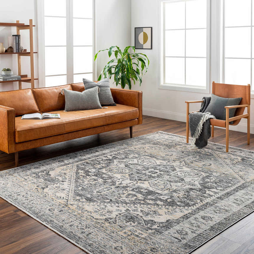 Living room scene with a brown leather sofa and Ailsa Area Rug in dark gray, lambswool, and brown tones. Roomscene-Rectangle