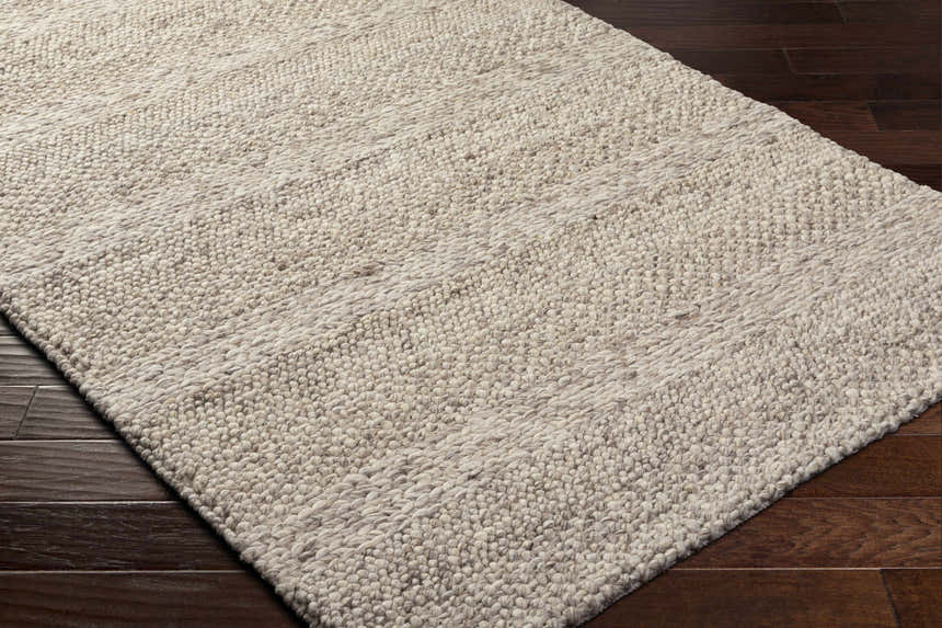Close-up of the hand-woven Mitzy Area Rug. Beige and bone wool rug with a farmhouse style and textured design. Corner