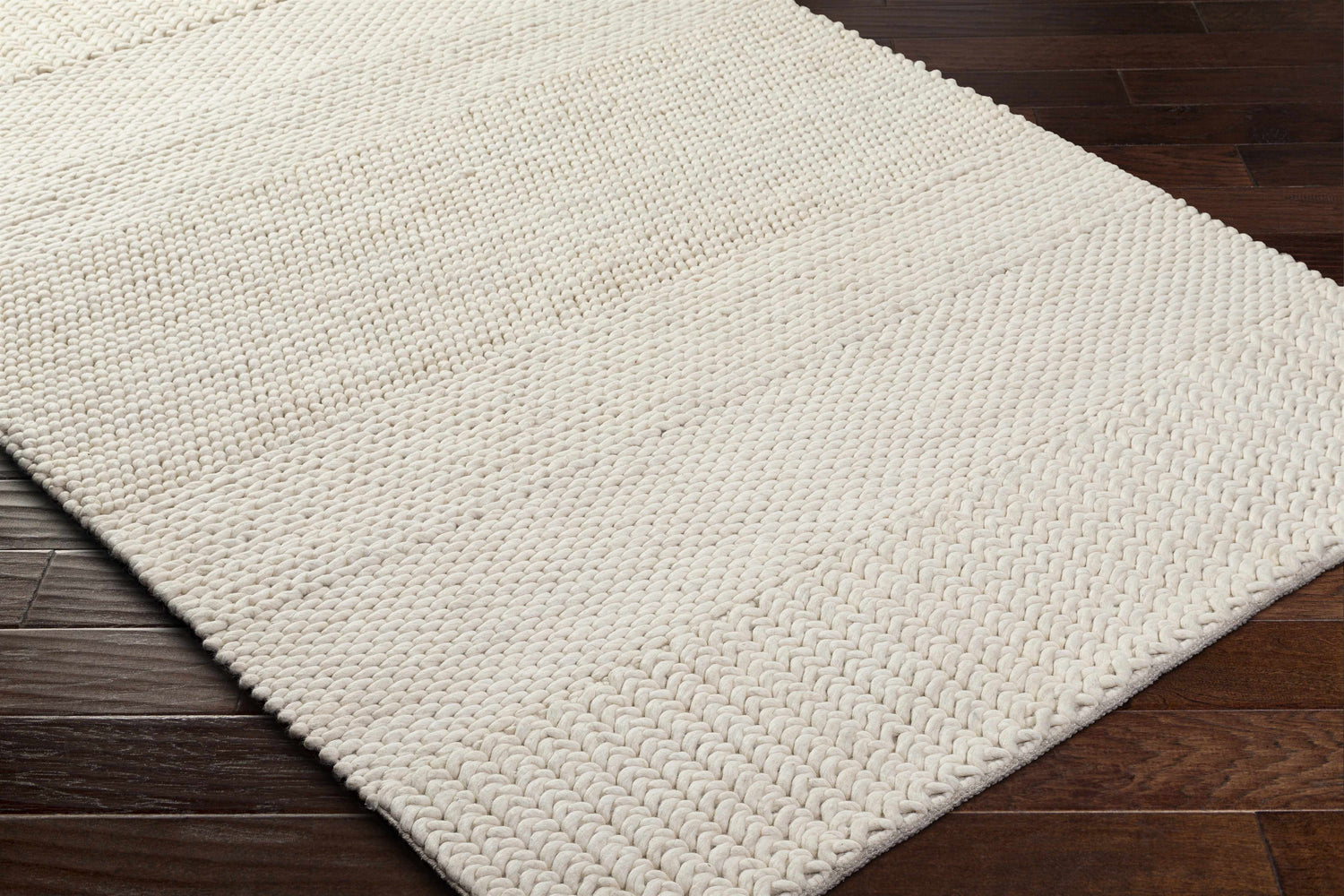 Close-up of the hand-woven Nimai Cream Wool Area Rug showing its texture and design on a dark wood floor. Corner