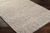 Close up of the hand woven Nimai Beige Wool Area Rug showing texture and detail on dark wood floor. Corner