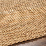 Close-up of the caramel-colored Olof Hand Woven Jute Rug showing texture and hand-woven construction on wood floor. Texture