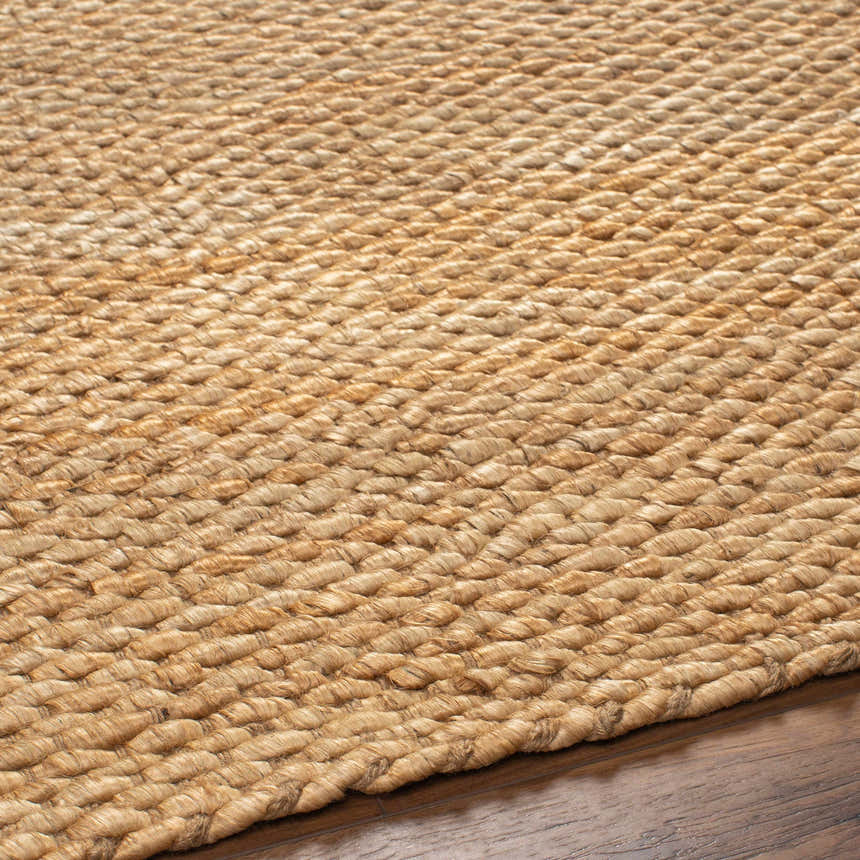 Close-up of the caramel-colored Olof Hand Woven Jute Rug showing texture and hand-woven construction on wood floor. Texture