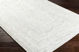 Close-up of the hand-woven Kenyi Rose Cream Area Rug showing its beige, gray, and white texture on dark wood floors. Corner