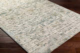 Close-up of the Chaka Textured Rug. Features a contemporary design in off-white, teal, and mustard on a dark wood floor. Corner