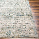 Close-up of the Chaka Textured Rug. Off-white rug with a distressed geometric pattern in teal, mustard, and gray on wood floors. Front