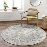 Living room scene with round Chaka Textured Rug in light gray, blue, and mustard tones. Wicker chair and wood side table. Roomscene-Round