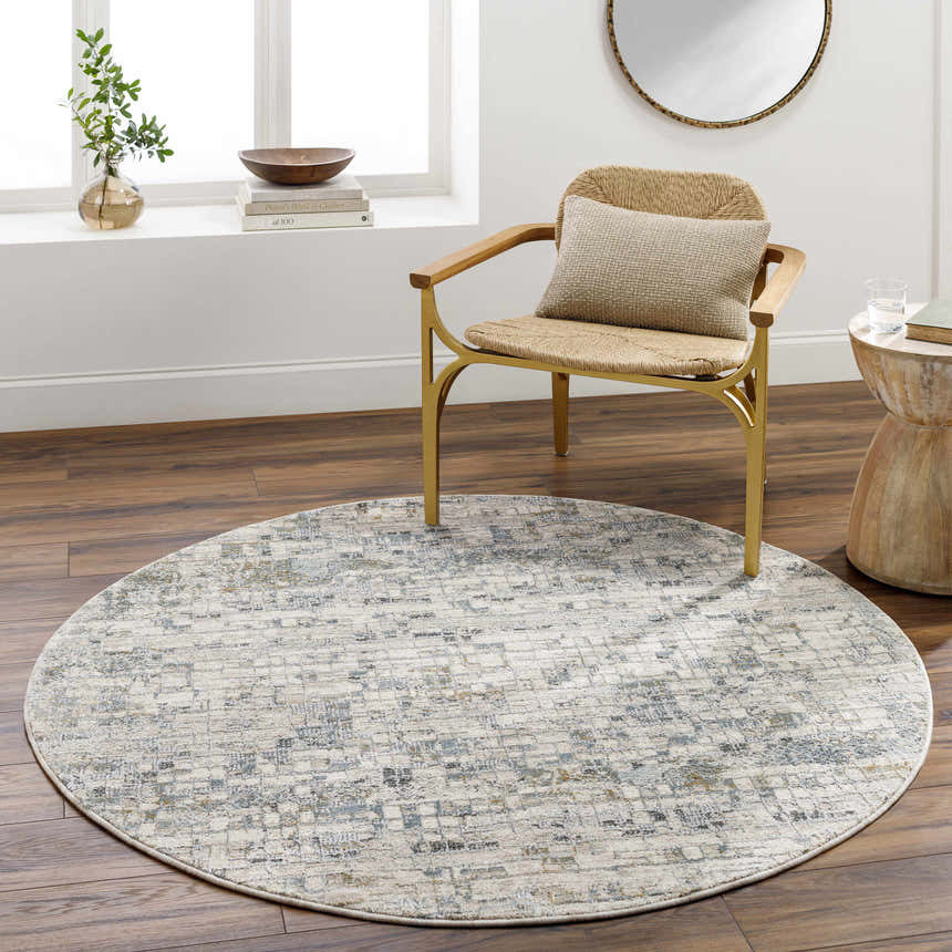 Living room scene with round Chaka Textured Rug in light gray, blue, and mustard tones. Wicker chair and wood side table. Roomscene-Round