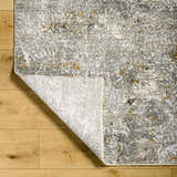 Close-up of Moke Textured Rug in gray, camel, and clay on wood floor, showing abstract design and construction. Fold