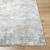 Close-up of Moke Textured Rug with Fringes. Abstract design in gray, white, and gold tones on a wood floor. Front