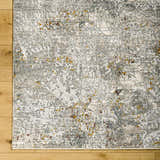 Close-up of Moke Textured Rug with Fringes. Abstract design in gray, light gray, and gold tones on a soft polyester rug. Corner