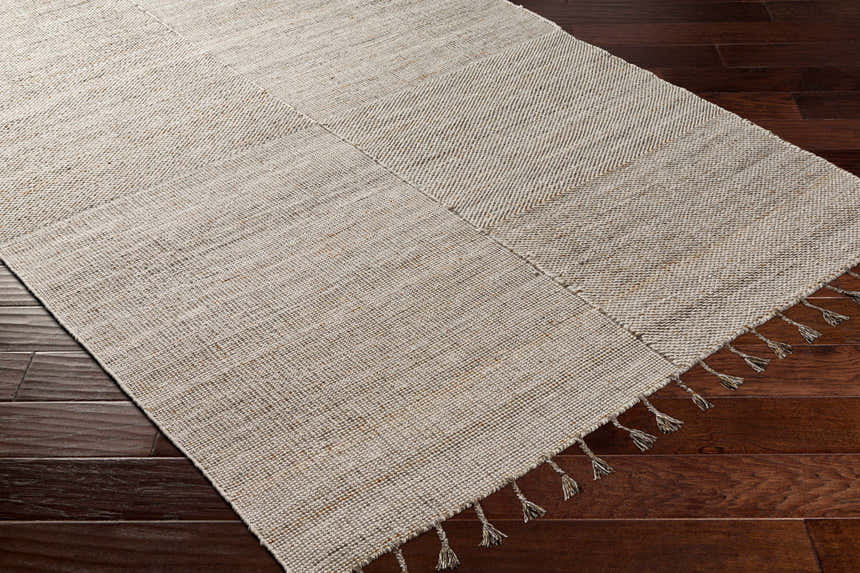 Close-up of the hand-woven Anaya Beige Area Rug on dark wood floors, showing texture and tassels. Corner