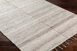 Close-up of hand woven Anaya Beige Area Rug with subtle pattern and tassels on dark wood floor. Farmhouse style. Corner
