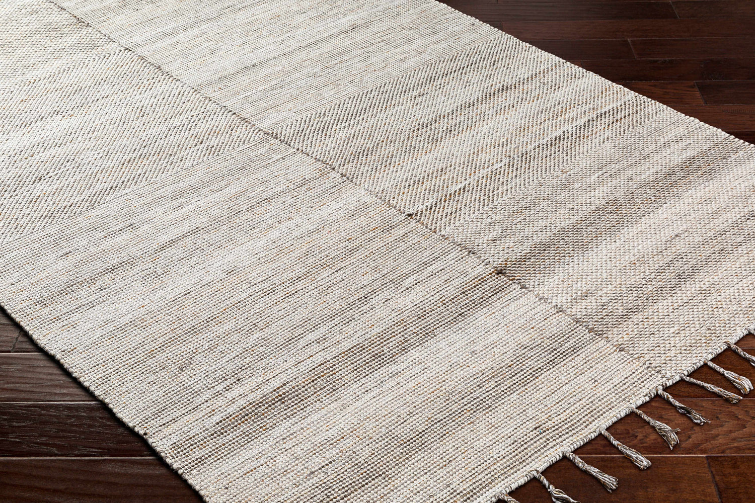 Close-up of hand woven Anaya Beige Area Rug with subtle pattern and tassels on dark wood floor. Farmhouse style. Corner