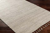Close up of the Anaya Beige Area Rug showing its hand woven texture and tassel detail on dark wood floor. Corner