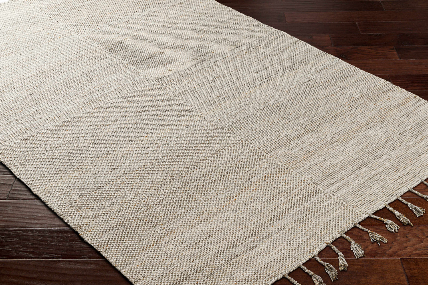 Close up of the Anaya Beige Area Rug showing its hand woven texture and tassel detail on dark wood floor. Corner