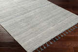 Close-up of the hand-woven Anaya Cream & Blue Area Rug with subtle stripes and blue tassels on dark wood floors. Corner