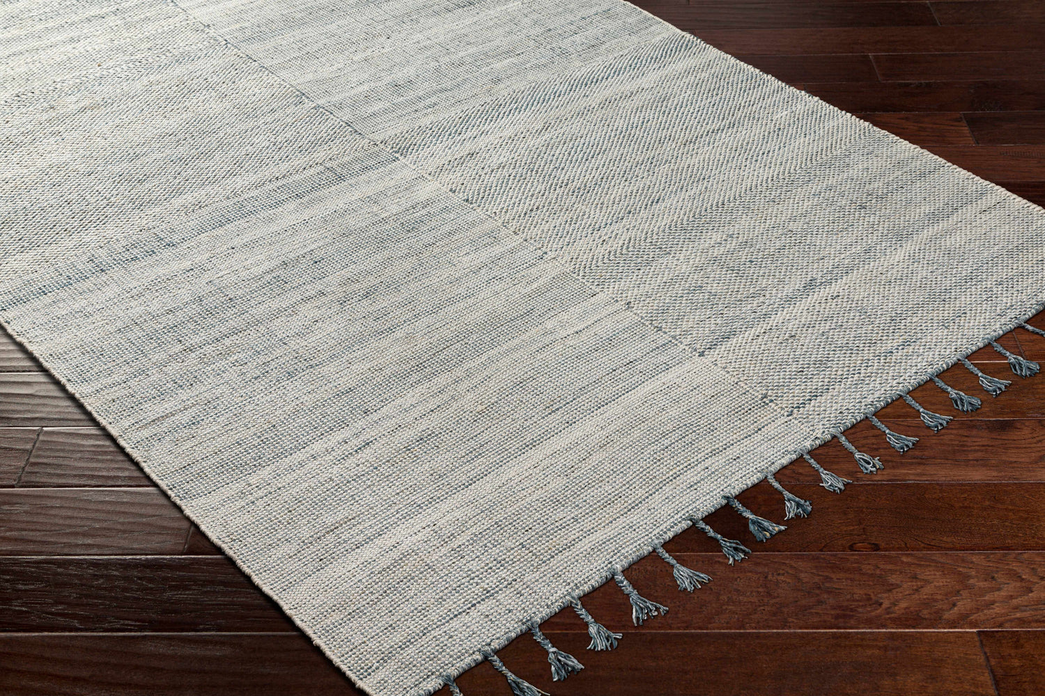 Close-up of the hand-woven Anaya Cream & Blue Area Rug with subtle stripes and blue tassels on dark wood floors. Corner