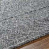 Close-up of the hand-woven Kyung Dark Gray Area Rug showing its texture and subtle geometric pattern on a wood floor. Texture