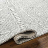 Close-up of the hand woven Kyung Gray Area Rug showing its light gray color, texture, and geometric pattern. Fold