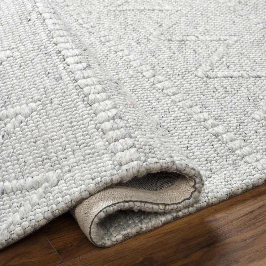 Close-up of the hand woven Kyung Gray Area Rug showing its light gray color, texture, and geometric pattern. Fold