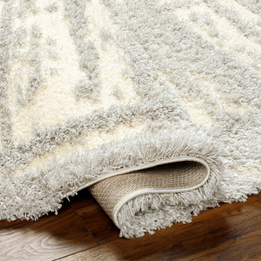Close-up of the plush Gidja Gray Area Rug showing its shaggy texture and geometric pattern in beige and gray tones. Fold
