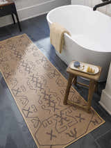 Bathroom scene with a camel Hamid Washable Jutely Rug runner, white tub, dark tile floor, and rustic wood stool. Roomscene-Runner