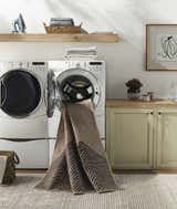 Laundry room scene with a Suzy Washable Jutely Rug partially inside a washing machine, showing its camel and charcoal pattern. Washing-Machine