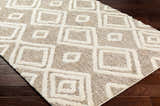 Close-up of the Nima Area Rug on dark wood floors. Bone and tan shag rug with a geometric square pattern. Corner
