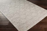 Close up of the hand woven Sauget Area Rug in off white and gray on a dark wood floor. Corner
