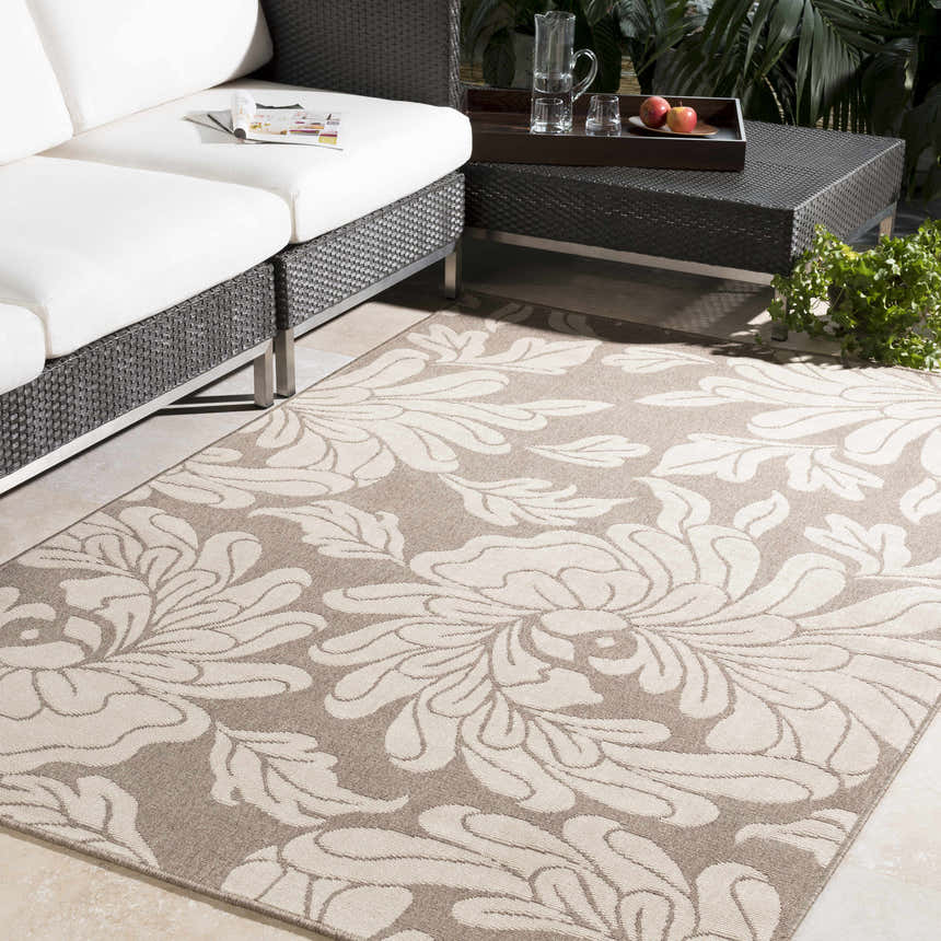 Outdoor patio scene with a beige floral Sherard Area Rug, white sofa, and dark wicker table. Roomscene-Rectangle