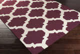 Close-up of the Shotton Area Carpet. Dark purple wool rug with an ivory geometric trellis pattern. Hand woven. Corner