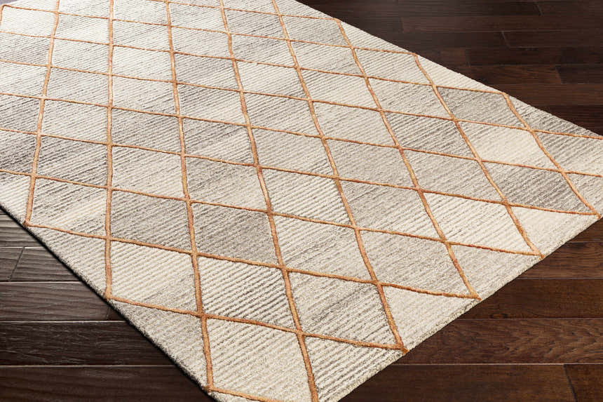 Close up of Sharpes Area Rug with brown, mustard, and orange geometric pattern on dark wood floor. Corner