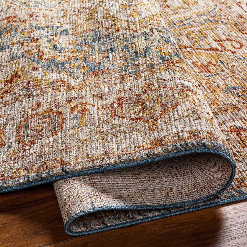 Close-up of the textured Cress Tan Rich Traditional Rug showing bone, blue, and rust colors and a folded edge. Fold