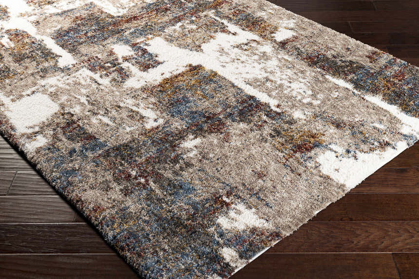 Close-up of the Silvis Boutique Area Rug showing its shag texture and abstract pattern with cream, gray, blue, and burgundy tones. Corner