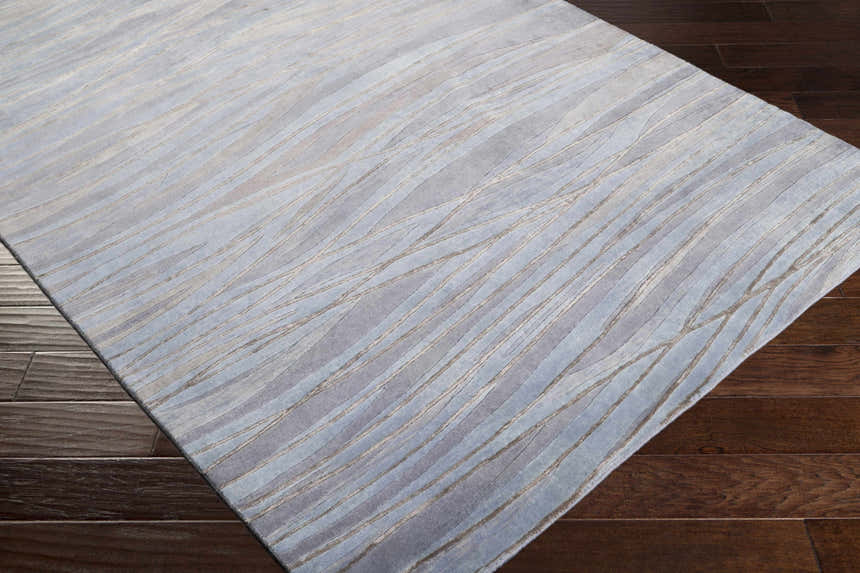 Close-up of Sinai Light Blue rug showing lined pattern and texture on dark wood floor. Wool and viscose rug. Corner